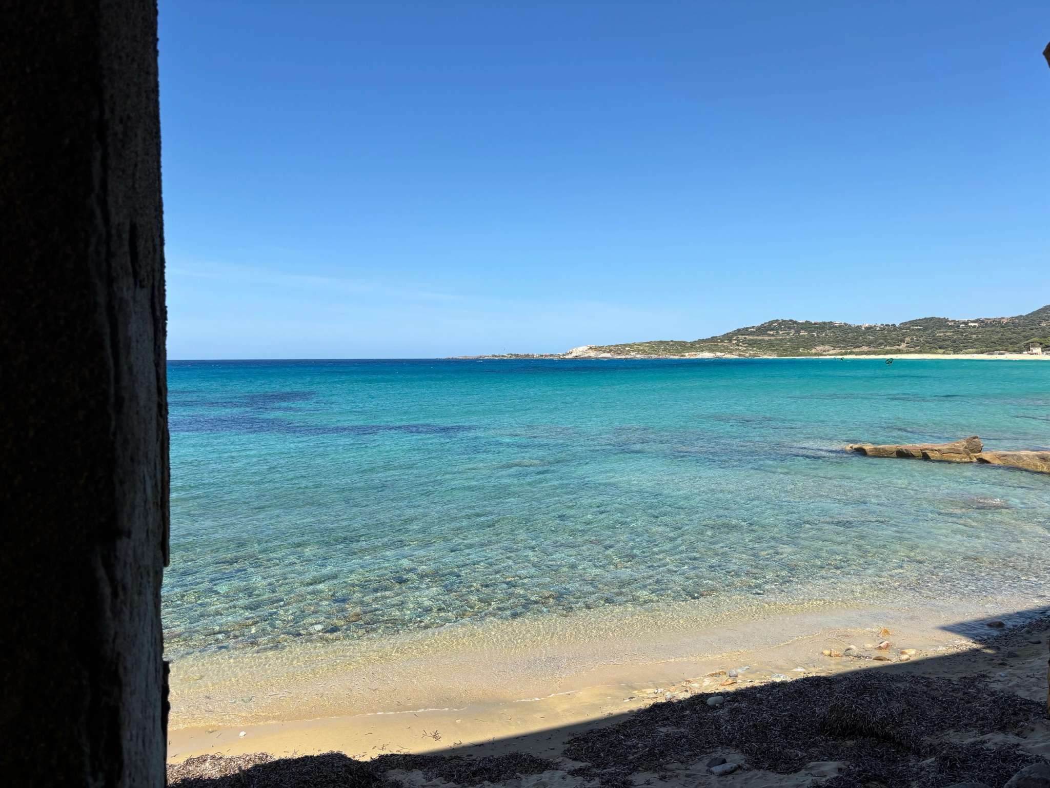 Plage méditerranéenne aux eaux turquoises et sables fins avec collines côtières en arrière-plan par beau temps